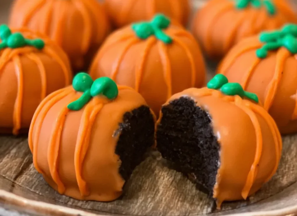 Decorative plate of pumpkin Oreo balls with candy stems and autumn leaves.