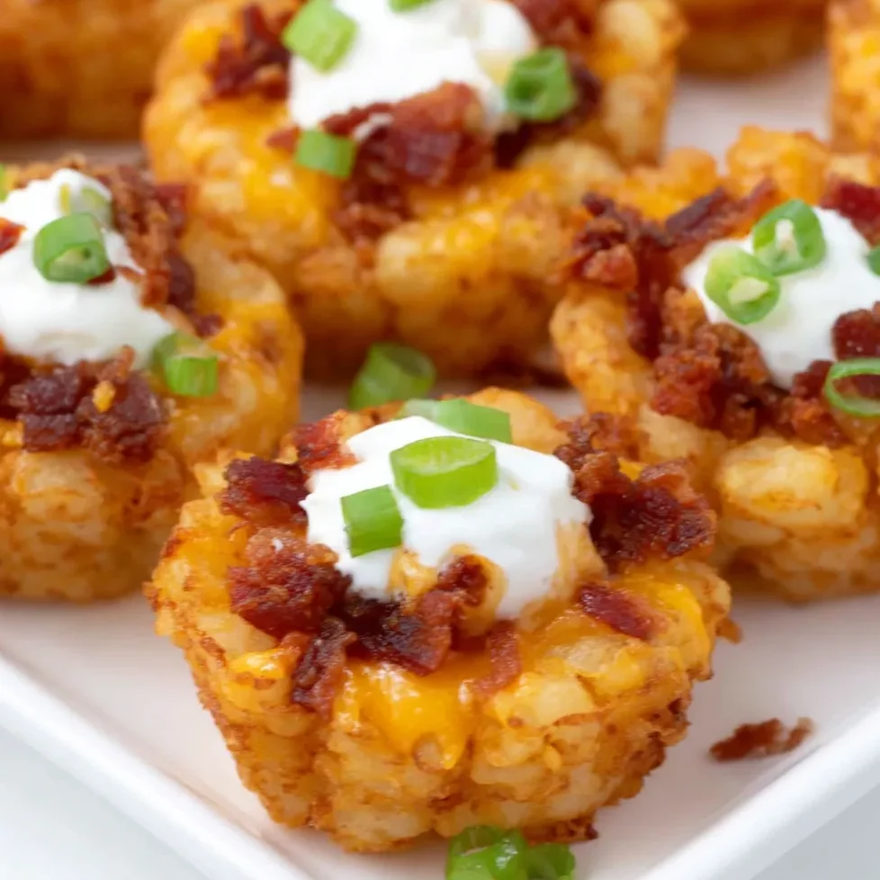Plate of loaded tater tots topped with melted cheese, sour cream, and green onions.