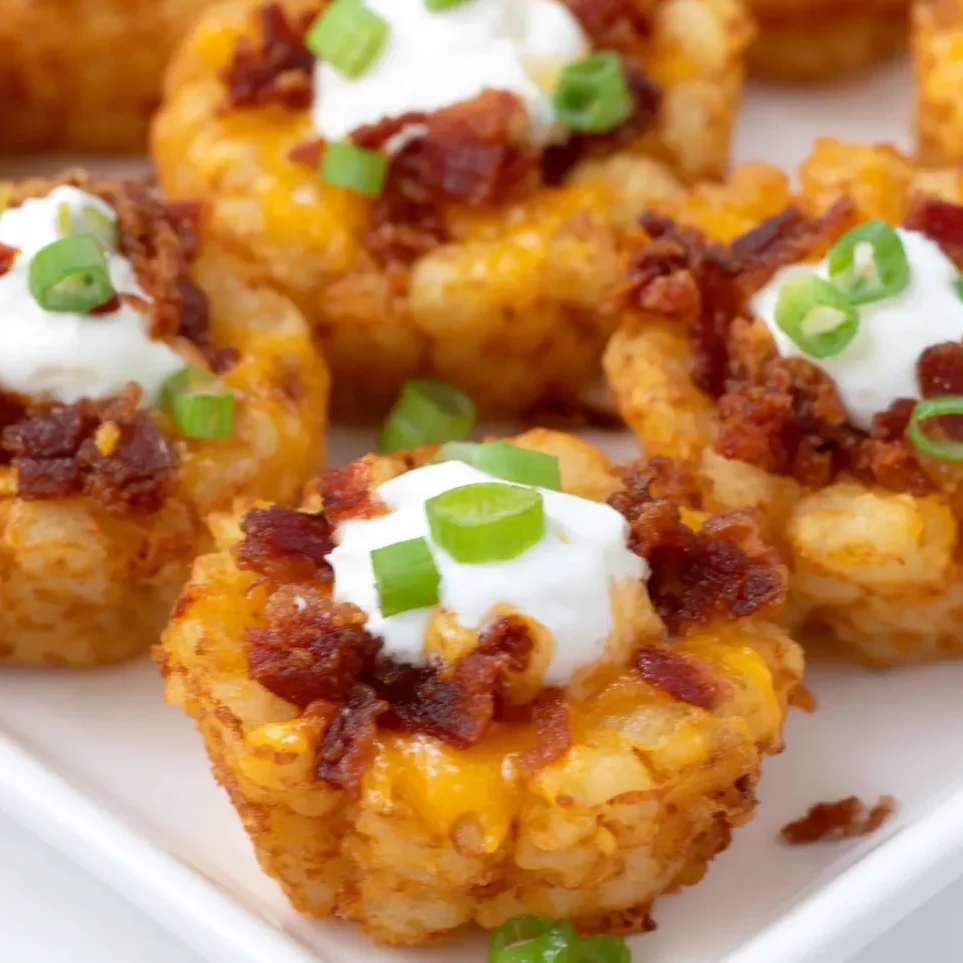 Plate of loaded tater tots topped with melted cheese, sour cream, and green onions.